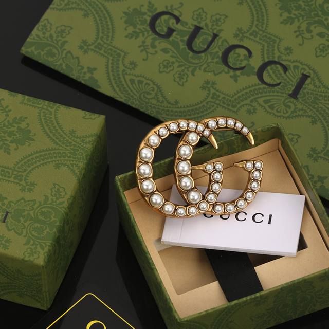 Gucci双g古驰胸针 作为品牌的标志性元素，运用品牌首字母以别致的方式呈现。金色效果金属标识与白色玻璃珍珠边框相得益彰，令整款设计更显精致典雅的气息。融合了品